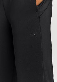 Schwarze Sportleggings mit schlankem Schnitt, glatter Textur, sichtbaren Nähten und einem kleinen silbernen Logo an der Seite.