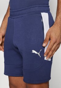 Marineblauwe sportshorts met een witte zijstreep, een elastische tailleband en een zilveren logo. Gemaakt van zachte, gestructureerde stof. Voorzien van zakken met rits.