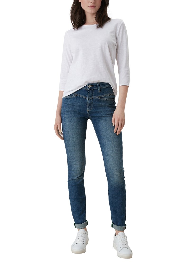 Blusa blanca de manga Tres Cuartos con cuello redondo, combinada con jeans skinny de mezclilla azules y zapatillas blancas, con puños enrollados.