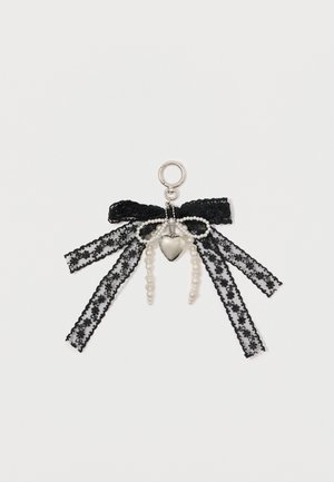 Black lace charm featuring a bow with silver hardware, pearl accents, and a heart-shaped pendant, showcasing intricate patterns and layered ribbons.