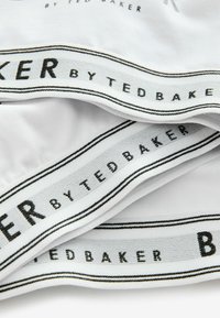 Hvidt stof med en sort og sølv talje, der viser teksten "by TED BAKER," med en glat tekstur og rent design.