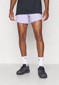 Helle lila Sportshorts, schwarzes T-Shirt, weiße Socken und schwarze Turnschuhe. Die Shorts haben eine glatte Textur und ein Nike-Logo an der Seite.