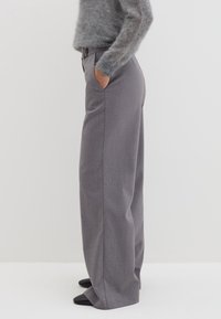 Grijze high-waisted, wijde broeken met zijzakken, textuurstof en strakke lijnen, gecombineerd met zwarte puntige schoenen.
