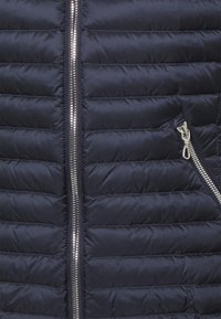 Granatowa kamizelka puchowa z poziomym pikowaniem, srebrnym zamkiem błyskawicznym i boczną kieszenią na zamek. Gładka faktura i lekki materiał.