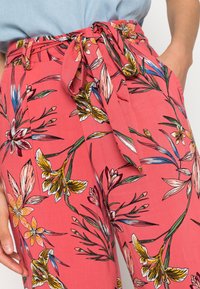 Pantalons floraux roses avec une ceinture attachée à la taille. Présente des motifs de fleurs jaune vif et vert sur un tissu doux.