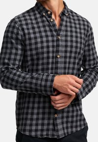 Czarna i szara flanelowa koszula w kratkę z kołnierzykiem na guziki i drewnianymi guzikami; miękka faktura i długie rękawy, dopasowane na nadgarstku.