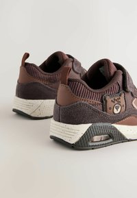 Brune ruskind- og lædersneakers med et struktureret overmateriale, prydet med et bjørneemblem, spraglede hvide mellemsål og sort gummisål.