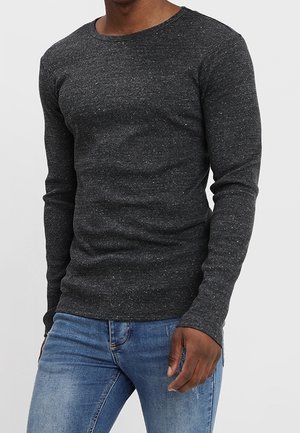 Camiseta de manga larga de color gris oscuro con cuello redondo, hecha de una tela de punto texturizada con un patrón discreto de moteado, combinada con vaqueros azules.
