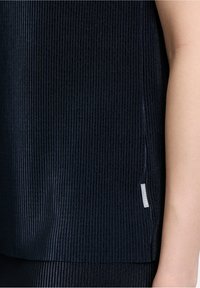 Navy blauwe geribde top met een gestructureerde afwerking, voorzien van een zijsplit en een klein merketiket aan de zoom. De stof lijkt zacht en rekbaar.