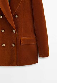 Blazer croisé en velours côtelé marron avec boutons dorés, poche latérale et tissu texturé. Coupe ajustée avec revers crantés.