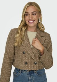 Veste courte en tissu marron texturé avec fermeture à double boutonnage, dotée de grands boutons noirs et d'un col cranté.
