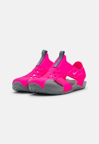 Sandalias de color rosa neón con diseño abierto, suela texturizada en gris, tira de sujeción y pequeños agujeros de ventilación para transpirabilidad. Logotipo de Nike en el lateral.