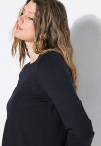 Mustat pitkähihainen paita, jossa on pyöreä kaula-aukko ja sileä pinta, näyttäen istuvaa muotoilua ja sivusaumadetaileja.
