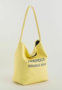 Geel, gestructureerde schoudertas met een slungelige vormgeving, met de tekst "FRIENDLY DOUBLE BAG" in zwart op de voorkant.