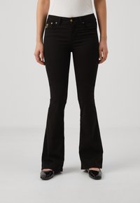 Musta liehuhousut, joissa on istuva vyötärö ja viiden taskun malli. Koristeena kullanväriset metalliosat ja hillitty logopatchi takataskussa.