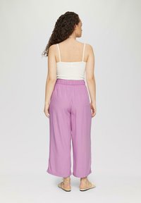 Pantalons larges violet clair avec une taille élastique, associés à un débardeur blanc à côtes. Tissu texturé, design décontracté.