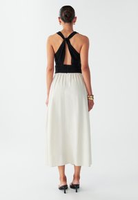 Maxikleit, millel on must tekstuuriga ülaosa keeratud rihmadega, avatud seljaga ning voolava koorevärvi seelikuga. Sile kangas, minimaalsed aksendid.