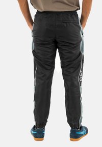 Pantaloni sportivi neri con rifiniture teal ai lati, vita elasticizzata e polsini alle caviglie. Presentano un logo e una tasca con zip nella parte posteriore per riporre gli oggetti.