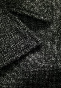 Tejido texturizado en gris oscuro con un sutil patrón moteado. El material parece suave y tejido, mostrando fibras y bordes visibles.