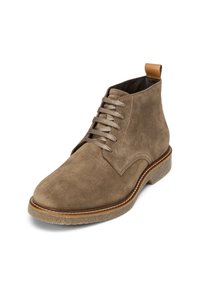 Bottine en suède marron avec un bout arrondi, un laçage sur le devant et une languette en cuir beige, dotée d'une semelle en caoutchouc texturé et de coutures contrastantes.