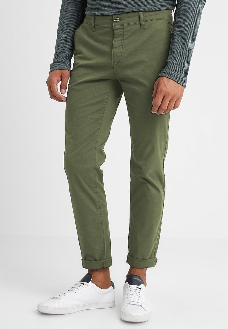 Olive green chinos made of cotton blend fabric, featuring a slim fit, front pockets, and cuffs rolled above the ankles paired with white sneakers.