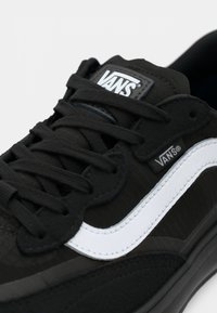 Svart Vans-sneaker med teksturert overdel, hvit side stripe, svarte snørebånd og logo-lapp på tungen. Har en gummisåle for godt grip.