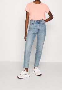 Růžové tričko s krátkým rukávem, světle modré džíny s vysokým pasem a bílé sportovní boty s červenými a černými akcenty, s komfortním střihem.