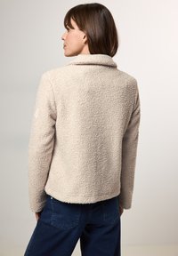 Beige, textuur fleece jack met een kraaglijn, getoond vanaf de achterkant. Heeft een iets cropped pasvorm en lange mouwen.