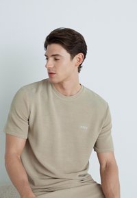 Khaki tričko s krátkym rukávom z jemnej bavlnenej zmesi, so zaobleným výstrihom a malým bielym logom "BOSS" na hrudi.