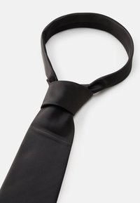 Cravate en soie noire avec un motif texturé en côtes. Présente un design noué et une extrémité lisse et plate pour une apparence soignée.