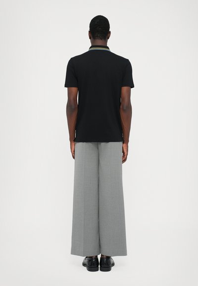 Polo negro de manga corta con un collar multicolor, combinado con pantalones de pierna ancha en gris claro. Zapatos negros visibles en la parte inferior.