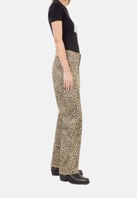Pantalones acampanados de estampado de leopardo en tonos beige y marrón, con cintura alta y una textura suave. Combinados con una camiseta ajustada negra.