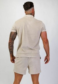 Beige frotté polo- och shortssats med korta ärmar och avslappnad passform. Enkelt mönster utan synliga mönster eller hårdvaruaccenter.