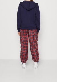 Sudadera navy con capucha ajustable, combinada con pantalones cargo de cuadros rojos y navy con puños elásticos y zapatillas blancas.