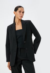 Blazer nero su misura con revers a sagoma, chiusura con un solo bottone e due tasche frontali. Tessuto morbido e vestibilità strutturata.