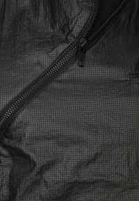 Czarna siateczkowa tkanina z wzorem kratki, z zamkiem błyskawicznym na jednym brzegu. Tekstura wydaje się lekka i pofałdowana.