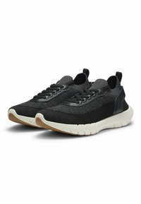 Chaussures de sport noires avec tige en mesh et tissu texturé ; dotées d'une semelle épaisse en caoutchouc blanc et d'un accent noir au talon.