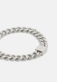 Bracciale in argento con una combinazione di maglie lisce e testurizzate, dotato di un moschettone rettangolare in metallo inciso con la scritta "BOSS."