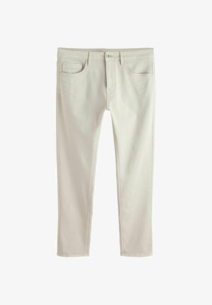 Vīriešu bēšas taujas pieguļošas džinsa bikses ar piecām kabatām, jostas cilpām, pogu aizdari un redzamām šuvēm, attēlotas uz baltas virsmas.