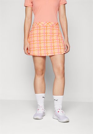 Jupe de tennis à motifs roses avec des accents orange ; présente un design plissé et une taille, associée à des chaussettes de sport blanches et des chaussures légères.