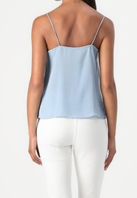 Haut à bretelles spaghetti bleu clair avec un ajustement ample, texture lisse et ourlet arrondi, associé à un pantalon blanc. Pas de motifs ni d'accents visibles.