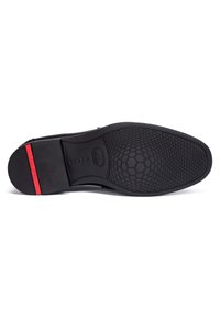 Schwarze Schuhsohle mit strukturiertem, hexagonalem Muster, das eine glatte Oberfläche und einen roten Akzent an der Ferse aufweist. Flache Form, langlebiges Material.