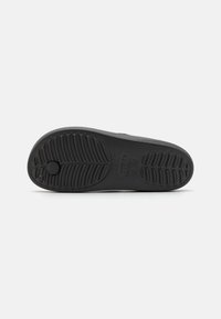 Semelle de chaussure en caoutchouc noir avec un motif de semelle texturé pour une meilleure adhérence. Présente une forme arrondie et un logo circulaire central prononcé.
