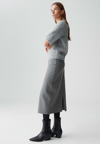 Grauer, flauschiger, kurzärmeliger Pullover kombiniert mit einem langen grauen Rock mit seitlichem Schlitz und schwarzen Stiefeletten mit spitzen Zehen.