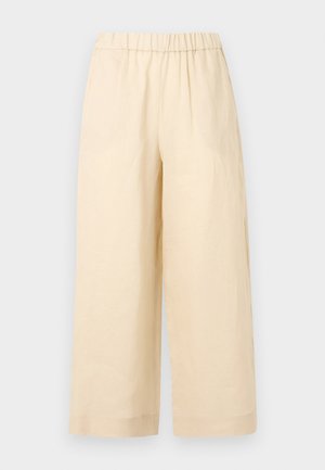 Béžové nohavice s širokými nohavicami, elastickým pásom a bez viditeľných vreciek, zobrazené na jednoliatom svetlom pozadí.