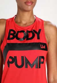 Rode atletische tanktop met grote zwarte opdrukken "BODY" en "PUMP", gemaakt van een glad, lichtgewicht materiaal en voorzien van een ronde halslijn.