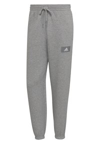 Šedé jogger kalhoty vyrobené z měkkého materiálu, s elastickým pasem a šňůrkou, sešnurovanými nohavicemi a malou logovou nášivkou na bocích.