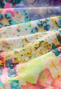 Wielokolorowa tkanina z kwiatowymi wzorami w odcieniach różu, niebieskiego, żółtego i zielonego, o teksturowanej powierzchni i miękkim układzie.