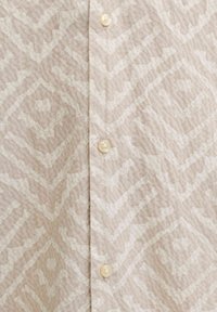 Chemise beige avec un motif géométrique subtil à base de formes en losange et trois boutons visibles couleur perle au centre.