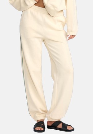 Cream-colored jogger pants with a relaxed fit, featuring side stripes and elastic waistband, paired with black slip-on sandals.